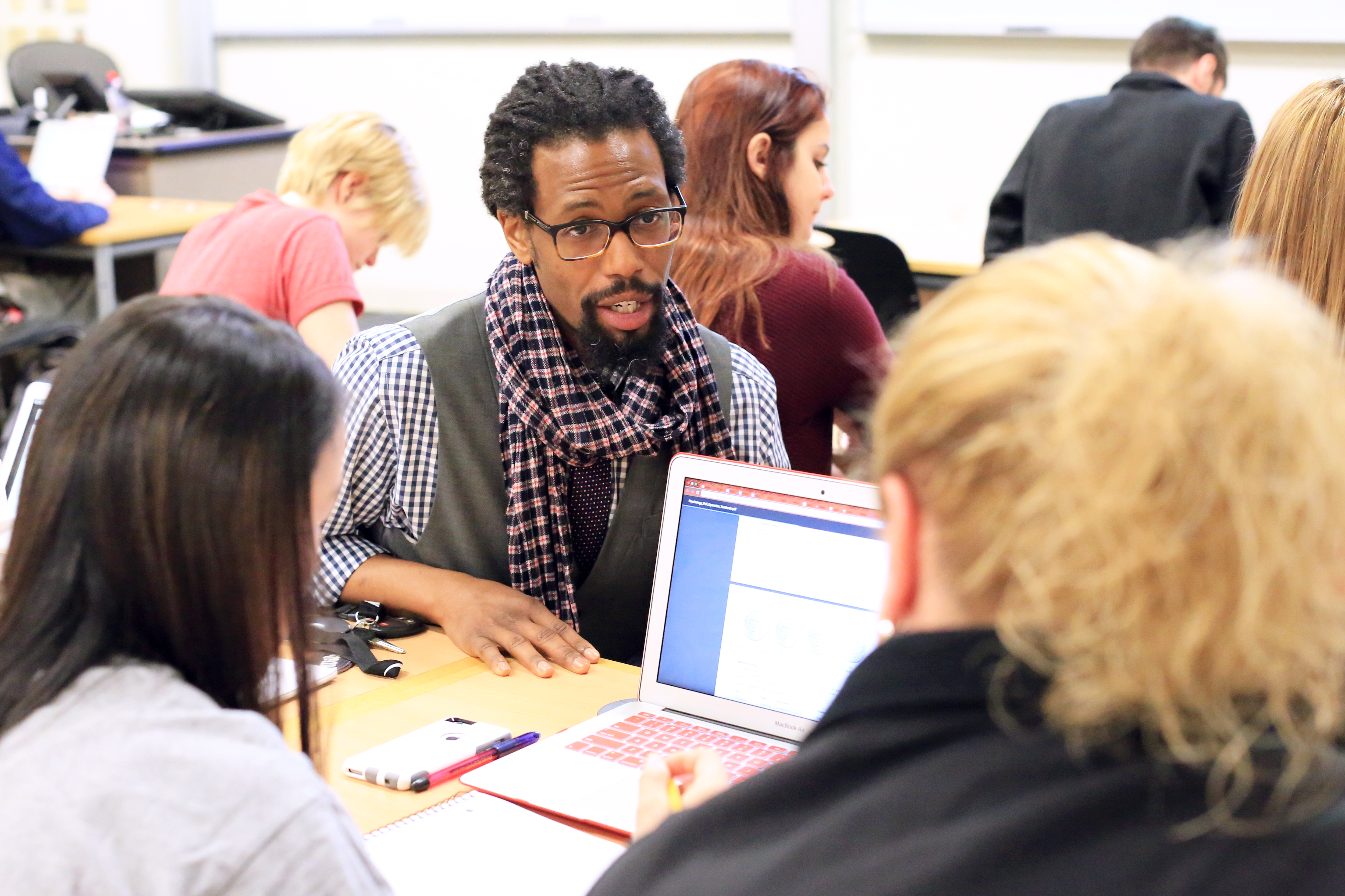 Male professor speaking with students who are looking at a laptop